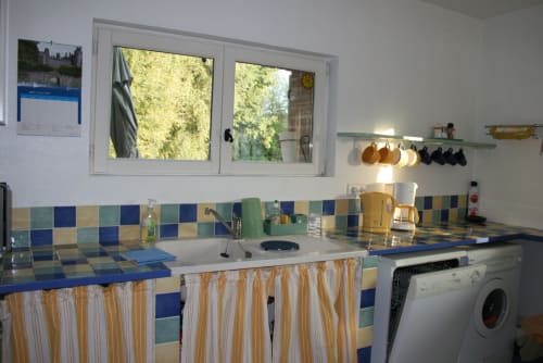 Bright kitchen at La Bouverie cottage with blue tile backsplash, washer, and window overlooking river