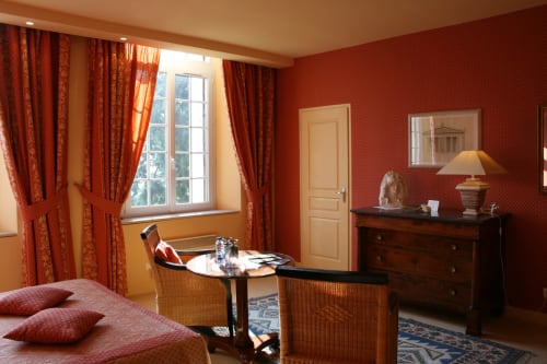 Elegant apartment bedroom at La Chatellenie with red damask walls, period furniture, and large windows with red curtains in