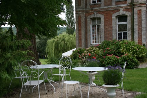 Elegant garden seating area at La Chatellenie with wrought iron furniture, blooming rose bushes, and brick manor house in