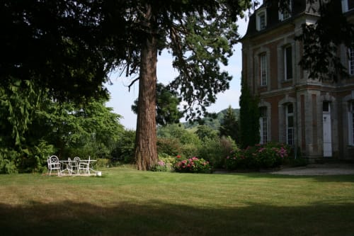 Le jardin de la Châtellenie avec ses sièges blancs sous les grands arbres, le manoir en brique et ses fleurs en fleur à Saint-Aubin-le-Cauf