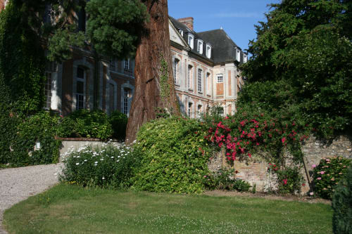 Cour de la Chatellenie avec bâtiments en pierre couverts de lierre, roses rouges en fleur, pelouse verte et architecture française