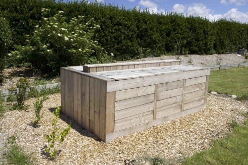 Wooden waste bin at Espace Ker Gana B&B in Plourin, France, surrounded by gravel and green hedges