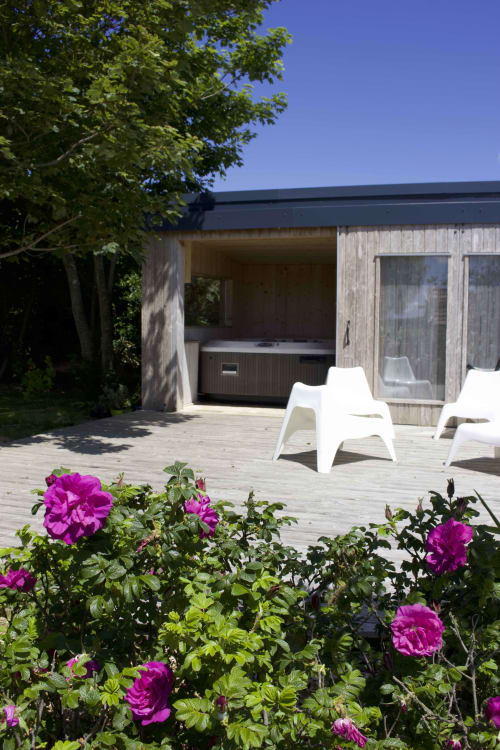 Magenta roses blooming on Espace Ker Gana's wooden deck with white chairs and spa tub in Plourin