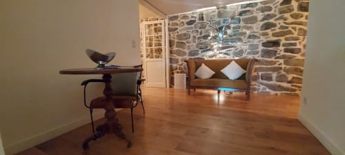 Chambre zen au Mas De Rigoulac avec sol en bois, mur de pierre, canapé en cuir avec coussins blancs et table vintage