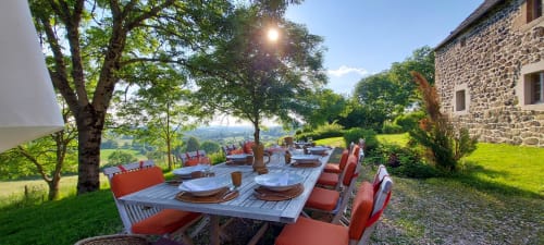 Terrasse de restaurant en plein air au Mas De Rigoulac en Aubrac avec vue sur le jardin, chaises rouges et bâtisse en pierre