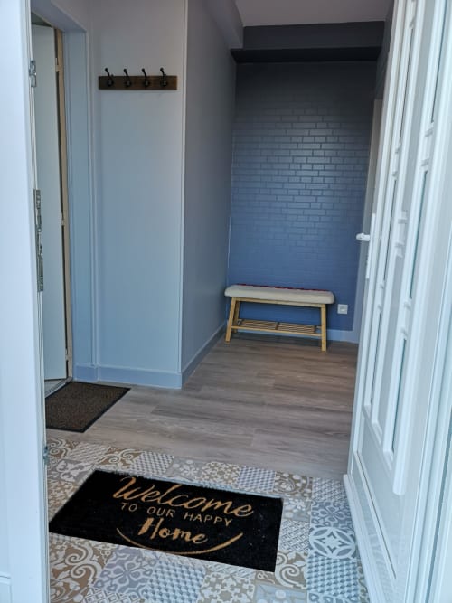 Modern entryway at Au Gîte d'Isigny cottage in Isigny-sur-Mer with welcome mat, wooden bench, and coat hooks