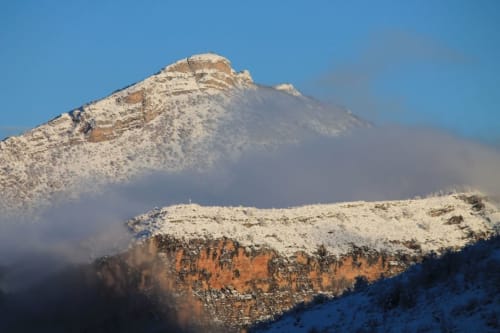 Pics de montagne enneigés près de Rémuzat avec formations rocheuses rouges et blanches stratifiées sous un ciel bleu clair