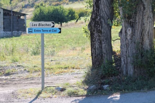 Panneau routier pour Les Blaches et le gîte Entre Terre et Ciel à Rémuzat, France, avec paysage campagnard et vieux arbres