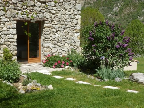 Jardin de charme à Entre Terre Et Ciel à Rémuzat avec fleurs violettes, allée en pierre et porte en bois