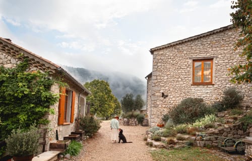 Cour en pierre du gîte Entre Terre Et Ciel à Rémuzat, avec bâtisses rustiques, lierre et vues montagneuses
