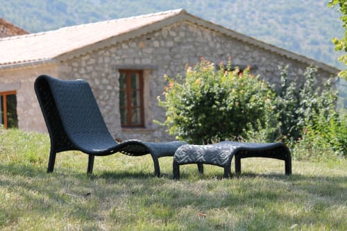 Fauteuil et ottoman noirs sur l'herbe à Entre Terre Et Ciel B&B à Rémuzat, France, avec maison en pierre en arrière-plan