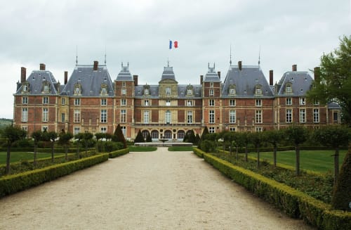 Imposant hôtel particulier du XIXe siècle, façade en brique rouge et toits mansardés, jardins entretenus et allée bordée d'arbres