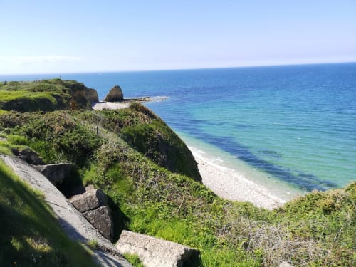 Coastal cliffs and pebble beach at Au Gite d'Isigny in Normandy with turquoise waters and green vegetation