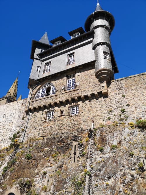 Historic stone tower of Au Gite d'Isigny B&B in Isigny-sur-Mer, France, with turret under clear blue sky