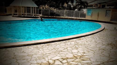 Piscine turquoise éclatante du Studio Face Marina à Saint-François avec terrasse en béton fissuré et clôture blanche, un nageur visible