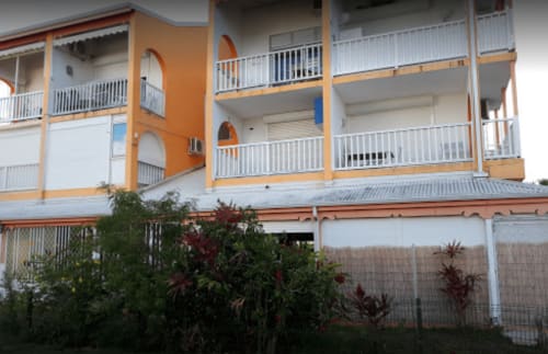 Façade de l'hôtel Studio Face Marina à Saint-François avec architecture orange et blanche, balcons et aménagement paysager tropical