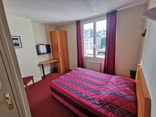 La Consigne hotel double room in Caen with pink bedding, wooden desk, flat-screen TV, and city views