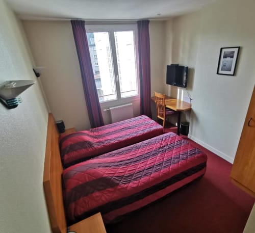 Twin bedroom at La Consigne hotel in Caen with red bedding, desk, flat-screen TV, and large window with purple curtains