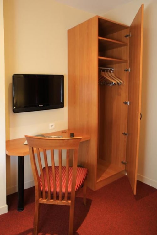 Twin room at La Consigne hotel in Caen with wooden desk, chair, wardrobe, and wall-mounted TV