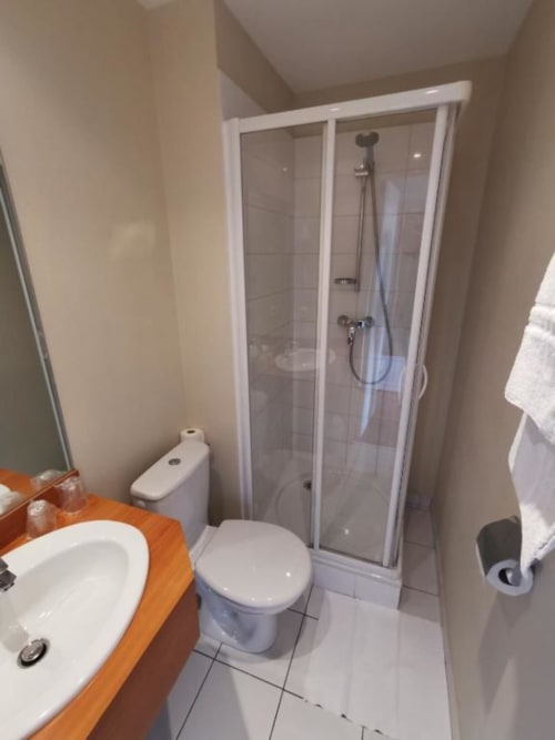 Twin room bathroom at La Consigne hotel in Caen with shower enclosure, toilet, and wooden sink vanity
