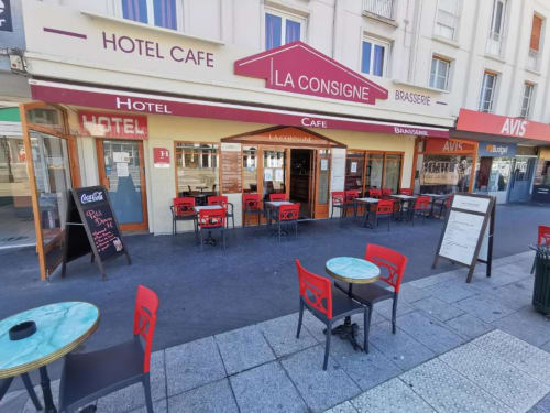 Hotel café La Consigne en Caen con sillas rojas y mesas azules en la terraza al aire libre
