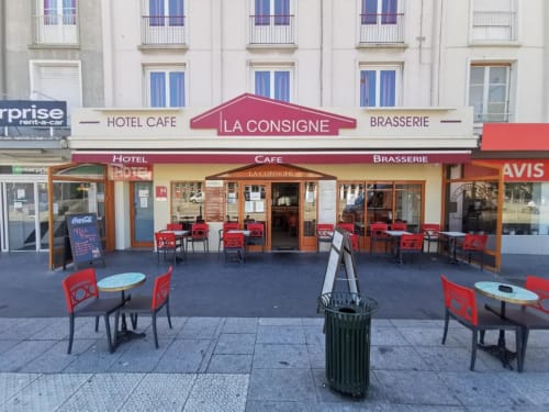Fachada de La Consigne Hotel Café Brasserie en Caen con sillas rojas y área de comedor al aire libre