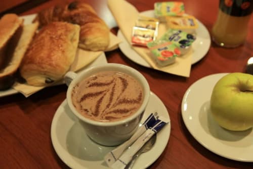 Desayuno continental en el hotel La Consigne de Caen con cappuccino decorado con latte art, pasteles, manzana y mantequilla