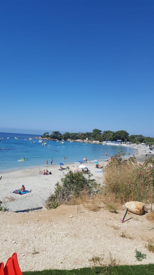Plage ensoleillée d'Ajaccio en Corse aux eaux turquoise, rivage sablonneux, bateaux et côte bordée d'arbres