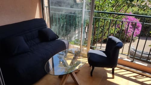 Balcon d'appartement moderne à Ajaccio avec mobilier noir, table en verre et vue mer sur jardins fleuris