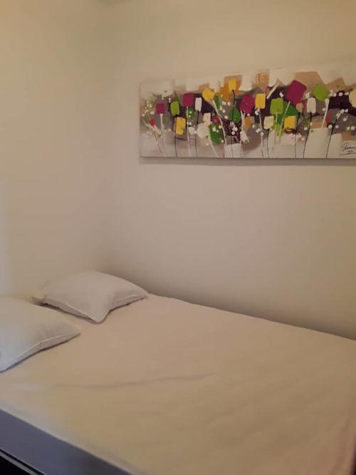 Chambre d'appartement corse avec vue sur mer, literie blanche, oreillers et décoration murale florale abstraite colorée