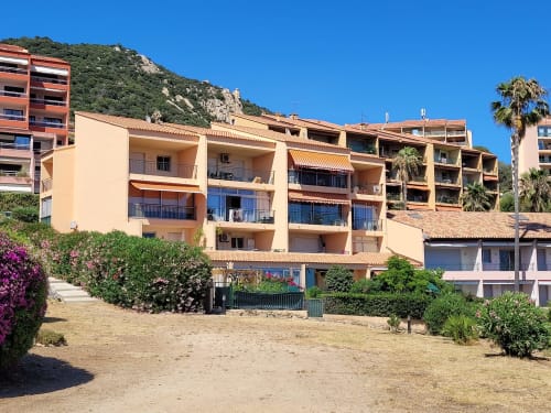 Location de vacances en bord de mer en Corse avec appartements aux toits en terre cuite, palmiers et paysage rocheux