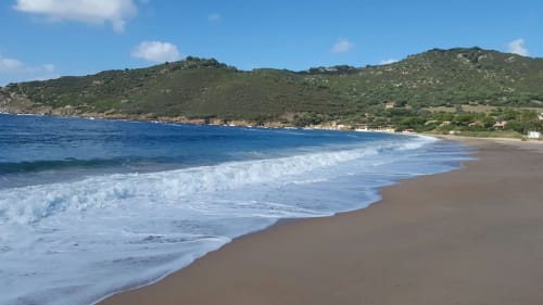 Plage de sable fin avec vagues turquoise et collines verdoyantes en Corse, France pour votre séjour