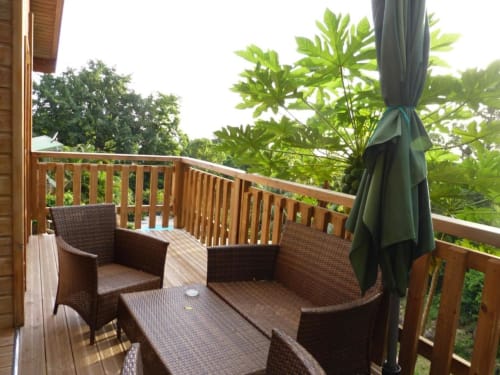 Bungalow con terraza de madera, asientos de ratán, paraguas, plantas tropicales y vistas al verdor en Le Bougainvillier Blanc