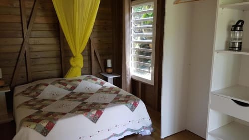 Wooden bungalow bedroom at Le Bougainvillier Blanc, Pointe Noire, with yellow curtains and patterned quilt
