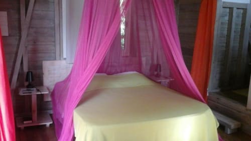 Cama con dosel romántica con cortinas de tul rosa en el bungaló Le Bougainvillier Blanc en Pointe Noire