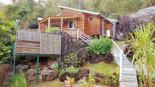 Wooden bungalow with covered porch nestled among rocks and tropical plants at Le Bougainvillier Blanc, Pointe Noire