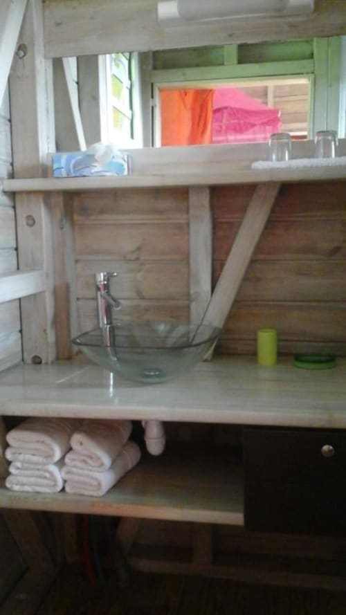 Mueble de baño de madera con lavabo y espejo en el bungalow Le Bougainvillier Blanc, toallas almacenadas debajo