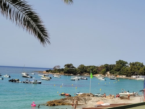 Petite crique corse aux eaux turquoise, bateaux amarrés, palmiers et plage de sable fin, idéale pour des vacances méditerranéennes.