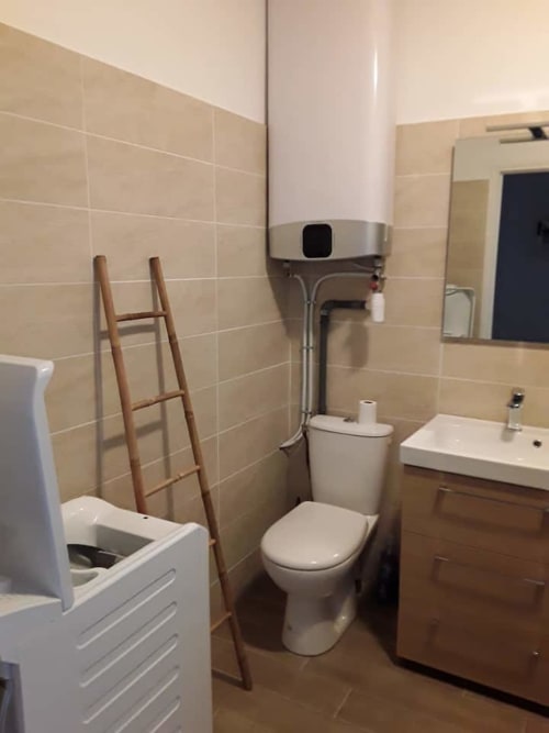 Salle de bain moderne dans un gîte corse avec toilettes blanches, lavabo, murs carrelés et porte-serviettes en bois