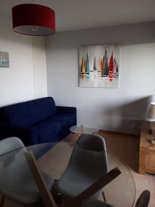 Salon moderne d'une maison d'hôtes corse avec canapé bleu marine, lampe suspendue rouge, tableau voilier et touches de bois