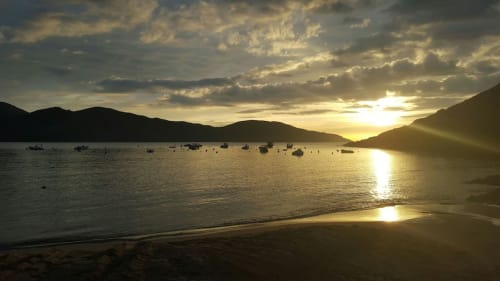 Coucher de soleil sur une baie corse avec bateaux amarrés, ciel doré se reflétant sur des eaux calmes, montagnes silhouettées à l'horizon