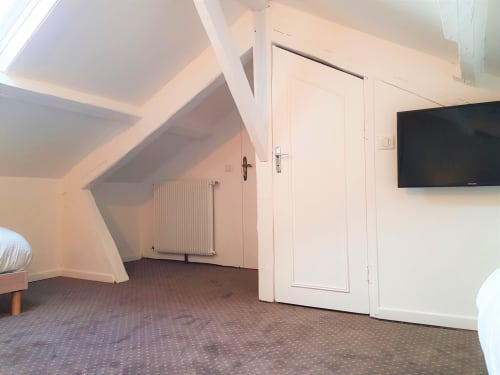 Chambre mansardée à l'hôtel Les Cabines à Houlgate avec plafond incliné, portes blanches, radiateur et TV murale