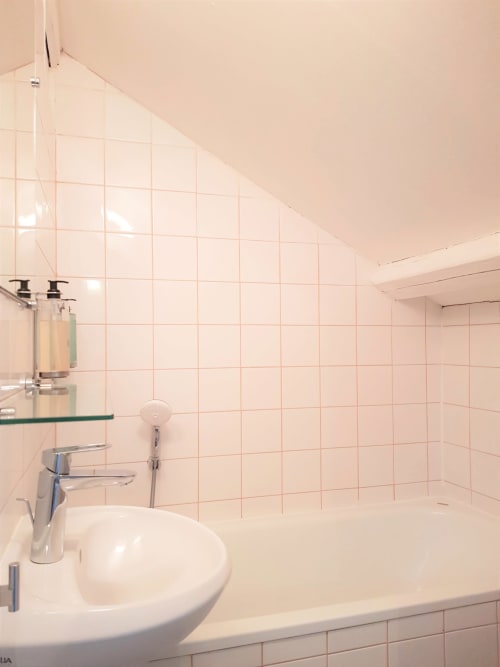 Salle de bain lumineuse avec lavabo rond blanc, robinetterie chromée et carrelage rose dans une chambre de l'hôtel Les Cabines, Houlgate
