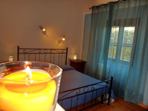 Accogliente camera da letto a Podere Oca Bianca con candele accese, letto in ferro battuto e vista sul giardino attraverso tende trasparenti