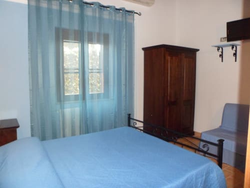 Camera luminosa a Podere Oca Bianca con letto blu, guardaroba in legno scuro e vista giardino attraverso tende leggere