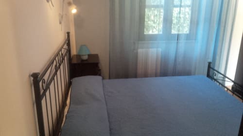 Camera luminosa a Podere Oca Bianca con biancheria blu, letto in metallo, finestre con vista sul giardino e arredamento rustico
