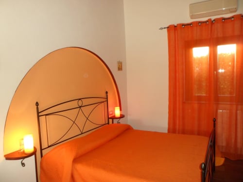 Camera da letto arancione luminosa con letto in ferro battuto, testata decorativa e vista sul giardino a Podere Oca Bianca, Pescia Romana