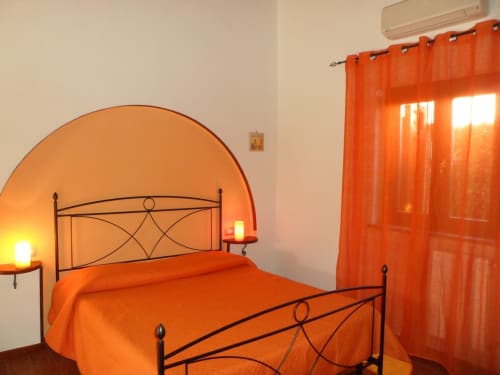 Camera da letto arancione brillante con letto in ferro battuto ornamentale e tende trasparenti a Podere Oca Bianca, Pescia Romana
