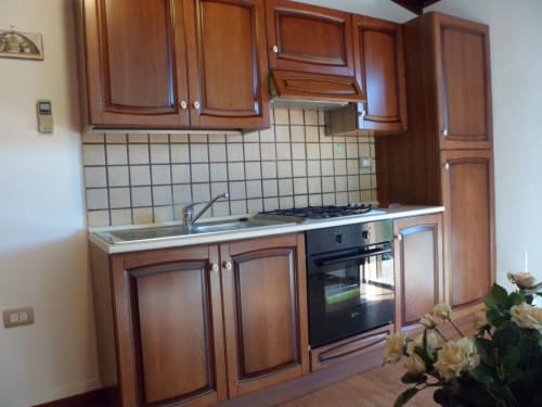 Cucina moderna con mobili in legno, fornello a gas, rivestimento in piastrelle bianche e lavello in acciaio inox nella camera Camelia a Pescia