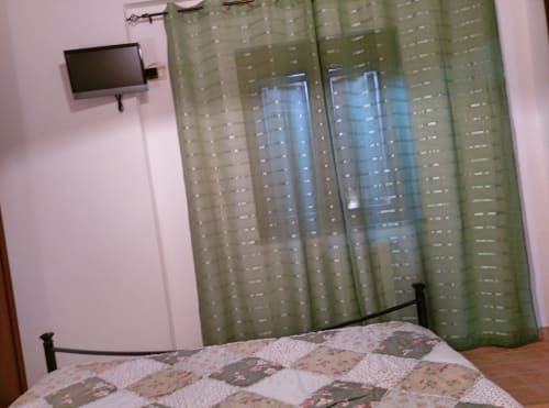 Camera Begonia al Podere Oca Bianca B&B a Pescia Romana con biancheria a motivi, tende verdi, TV a parete e arredamento in legno